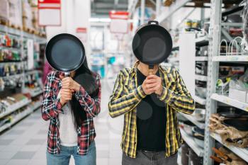 Young couple with frying pan instead of a head in supermarket. Male and female customers on family shopping. Man and woman purchasing goods for the house