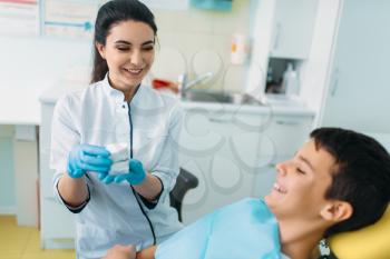 Female dentist shows dentures to little boy in a dental chair, professional pediatric dentistry, children stomatology