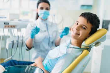 Smiling little boy in a dental chair, professional pediatric dentistry, children stomatology, female dentist on background