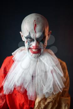 Portrait of mad bloody clown, face in blood. Man with makeup in halloween costume