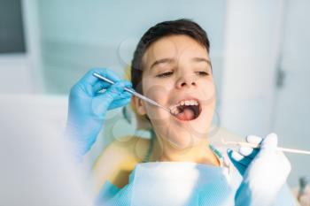 Boy with open mouth in a dental chair, pediatric dentistry. The doctor examines the teeth of a small patient