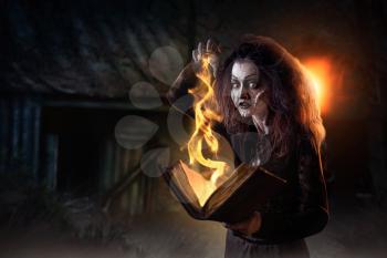Scary witch holds spellbook, dark powers of witchcraft, spiritual seance. Female foreteller calls the spirits, terrible future teller