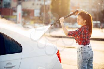 Cute woman on self service carwash. Outdoor vehicle washing at summer day. Female person with high pressure water gun