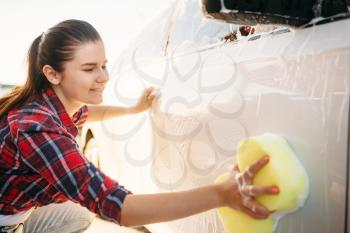 Young woman with sponge scrubbing vehicle with foam, car wash. Lady on self-service automobile washing. Outdoor carwash