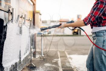 Female person with high pressure water gun in hands cleans car mats, touchless carwash. Young woman on self-service automobile washing. Outdoor vehicle cleaning at summer day 