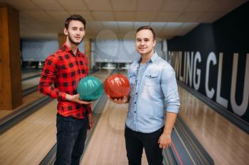 Two male bowlers poses on lane with balls on hands. Bowling alley players before competition. Classical tenpin game in club, active leisure