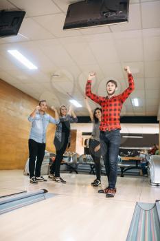Male bowler cheers holding hands up, he just makes strike shot. Bowling alley team congratulates each other, successful throwing. Men and women playing the game in club, active leisure