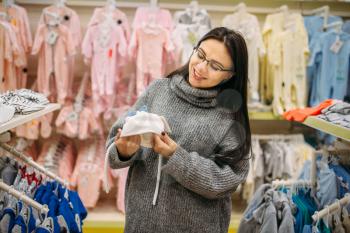 Smiling future mother chooses baby hat in the store for newborns. Pregnant woman in shop of goods for infants