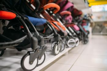 Row of baby strollers on shelf in store, nobody, goods for newborns. Pushchair variety in shop