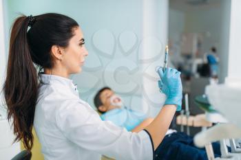 Female dentist with syringe of anesthesia, boy in dental chair, pediatric dentistry, children stomatology