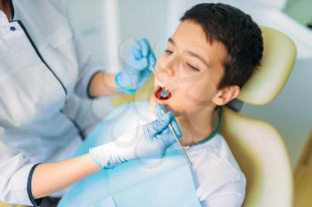 Boy with open mouth in a dental chair, pediatric dentistry. The doctor examines the teeth of a small patient