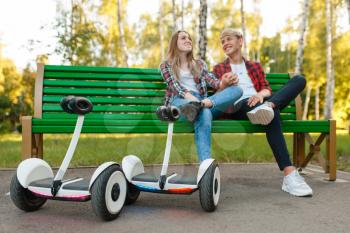 Young couple with gyroboard sitting on the bench in park. Outdoor recreation with electric gyro board. Transport with balance technology