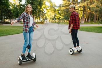 Young couple riding on mini gyro board in summer park. Outdoor recreation with electric gyroboard. Transport with balance technology