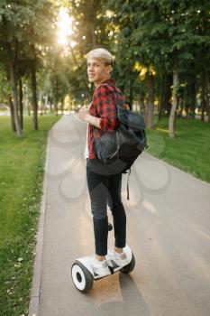Young man with backpack riding on mini gyro board in summer park. Outdoor recreation with electric gyroboard. Eco transport with balance technology, electrical gyroscope vehicle
