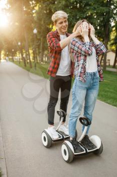 Young couple walking on gyro board in summer park. Outdoor recreation with electric gyroboard. Transport with balance technology