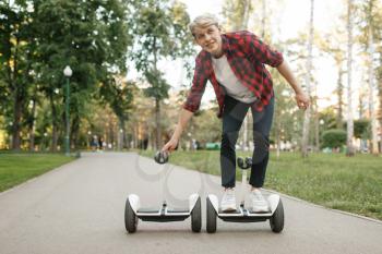 Young man riding on gyro board in summer park. Outdoor recreation with electric gyroboard. Eco transport with balance technology, electrical gyroscope vehicle