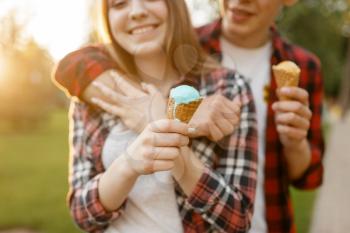 Young love couple with ice cream walking in summer park. Boyfriend and girlfriend leisures with ice-cream, romantic walk