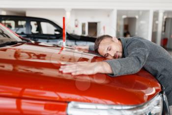 Man lying on the hood of new car in showroom. Male customer buying vehicle in dealership, automobile sale, auto purchase