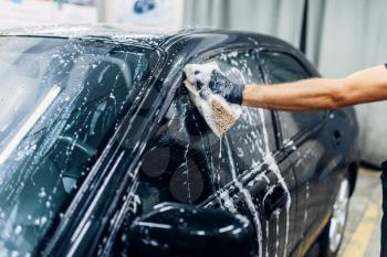 Carwash service, car cleaning, front view. Auto detailing, worker soaps glasses