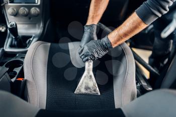 Professional dry cleaning of car interior with vacuum cleaner. Carwash service, male worker in gloves removes dust