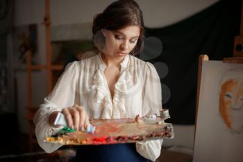 Female painter adds a color to the palette in studio. Creative paintbrush art, artist drawing portrait in class, workshop interior on background