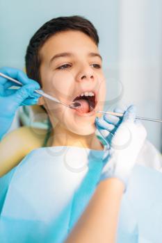 Little boy with open mouth in a dental cabinet, pediatric dentistry. Female dentist looking for caries