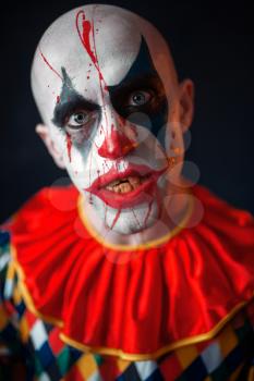 Portrait of mad bloody clown, face in blood. Man with makeup in halloween costume, crazy maniac 