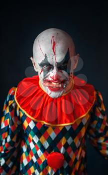 Portrait of mad bloody clown, face in blood. Man with makeup in halloween costume, crazy maniac