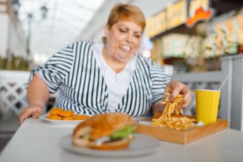 Fat woman eating high calorie food in mall restaurant. Overweight female person at the table with junk dinner, obesity problem