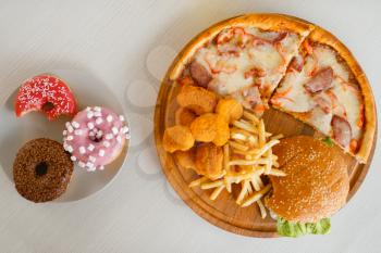High calorie food on the table, top view, nobody. Pizza and burger, doughnuts, french fries and chicken nuggets. Junk fastfood