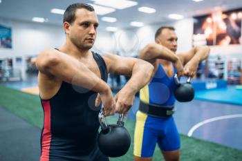 Strong male lifters doing exercise with kettlebell, lifting training in gym. Weightlifting workout in sport or fitness club