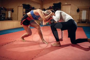 Female person holds the grip, self defense workout with male personal trainer, gym interior on background. Woman on self-defense training