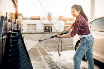 Young woman on self-service car wash. Outdoor vehicle washing at summer day. Female person with high pressure water gun