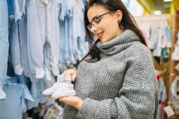 Happy future mother buys childrens clothes in the store for newborns. Pregnant woman in shop of goods for infants