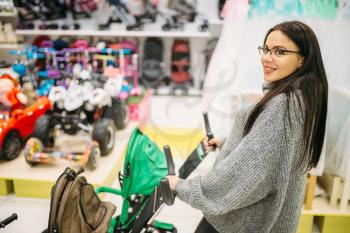 Pregnant woman poses with baby stroller in childrens goods store. Future mother choosing pushchair for her child, newborns transportation