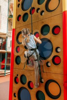Funny girl climbing walls in children game center. Excited child having fun on playground indoors. Female kid playing in amusement centre