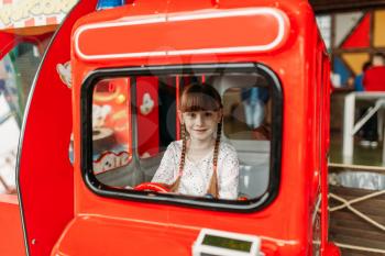 Little girl plays a bus driver, game machine, children entertainment center. Excited child having fun on playground indoors. Female kid playing in amusement centre