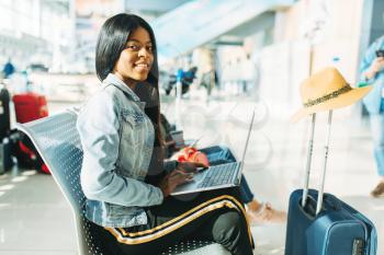 Female tourist with laptop waiting for departure in airport. Passenger with baggage in air terminal, happy journey of black lady, summer travel on vacation