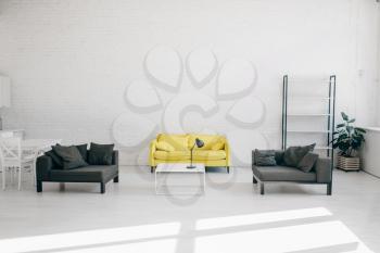 Modern living room interior in white, black and yellow tones, nobody. Cozy rest area with sofa, coffee table and empty shelf, comfort home design