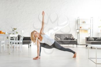 Yuong woman sitting on the floor in yoga pose, living room interior in white tones on background. Female person doing morning exercise, meditation