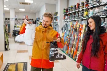 Couple choosing ski or snowboarding boots, shopping in sports shop. Winter season extreme lifestyle, active leisure store, customers buying skiing equipment