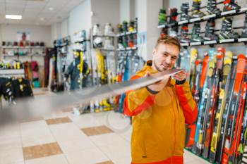 Man at the showcase checks the surface of the ski, shopping in sports shop. Winter season extreme lifestyle, active leisure store, customer buying skiing equipment