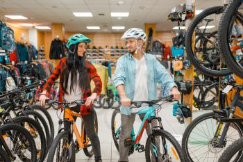 Couple in cycling helmets choosing bicycles, shopping in sport shop. Summer season extreme lifestyle, active leisure store, customers buying cycles