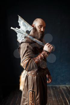 Angry viking with axe dressed in traditional nordic clothes, barbarian image. Ancient male warrior.