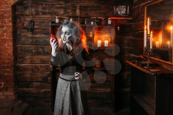 Scary witch holds human heart at the mirror and candles, dark powers of witchcraft, spiritual seance. Female foreteller calls the spirits, terrible future teller