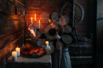 Scary witch reads spell over the pot, dark powers of witchcraft, spiritual seance with candles. Female foreteller calls the spirits, terrible future teller