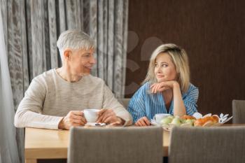 Breakfast of adult love couple at home. Mature husband and wife sitting in the kitchen, happy mature family, man and woman drinks coffee at the table with fruits
