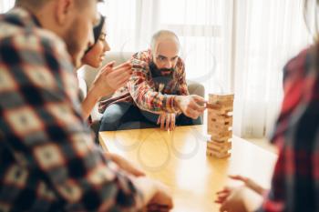 Friends plays table game at home, the man pulls wooden block from the tower. Board game requiring high concentration, entertainment for funny company