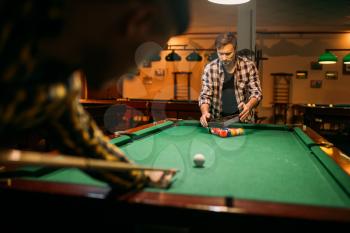 Two male billiard players with cue at the table with colorful balls. Men plays american pool in sport bar