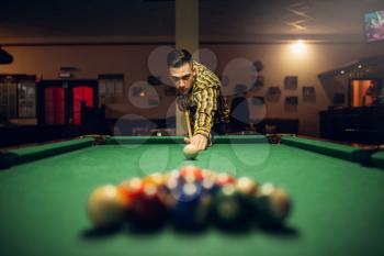 Male billiard player with cue aiming at the table with colorful balls. Man plays american pool game in sport bar